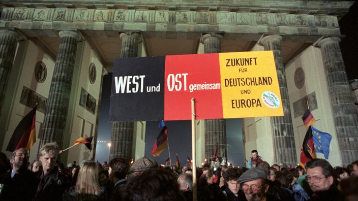 In einer Menschenmenge vor dem Brandenburger Tor steht auf einem Schild: "West und Ost gemeinsam. Zukunft für Deutschland und Europa"