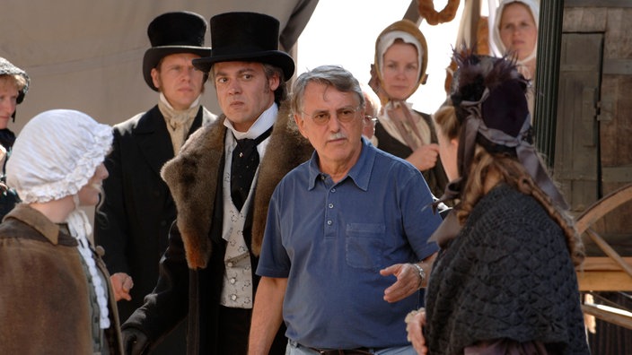 Regisseur Heinrich Breloer mit kostümierten Schauspielern am Filmset.