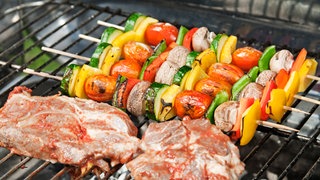 Gemüsespieße und Koteletts auf einem Grill.