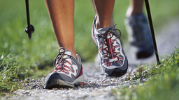 Frauenfüße mit Sportschuhen und Walking-Stöcken auf einem Kiesweg