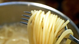 Spaghetti werden mit Gabel aus Kochtopf geholt