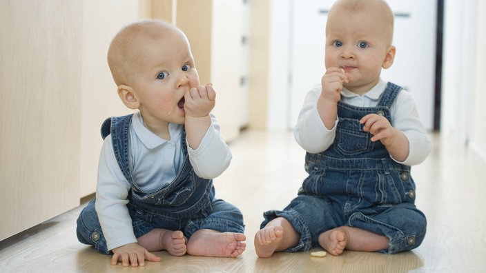 Zwillings-Babys sitzen auf dem Boden