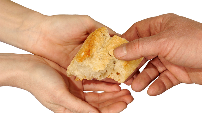 Zwei offene Hände halten ein Stück Brot, nachdem eine weitere Hand greift.