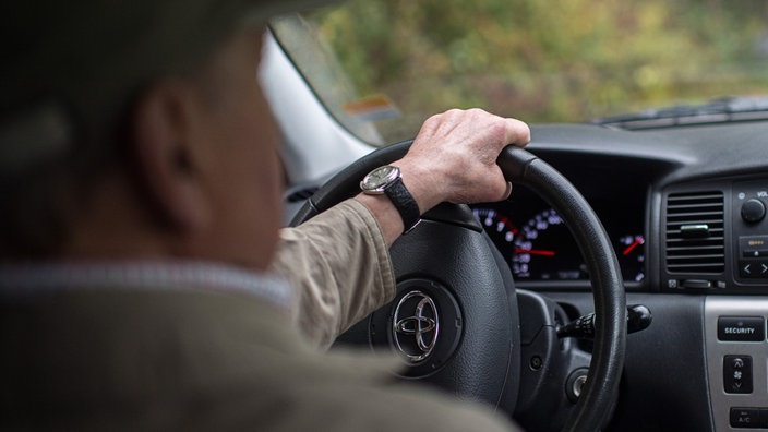 Ein älterer Herr sitzt im Auto und dreht das Lenkrad.