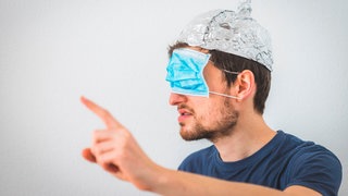 Ein junger Mann mit Aluhut auf dem Kopf und Corona-Maske vor den Augen