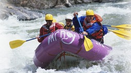 Männer in Schwimmwesten paddeln in einem Schlauchboot beim Wildwasser-rafting.