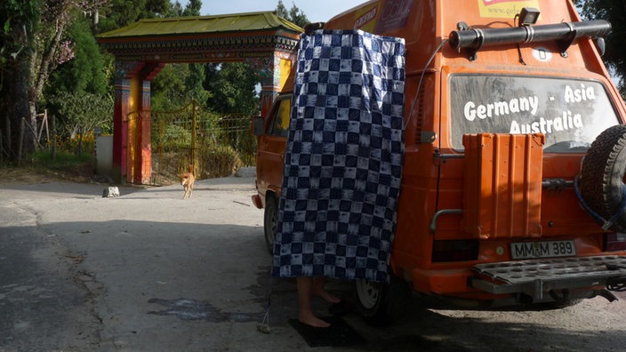 Frau duscht vor umgebautem VW-Bulli.