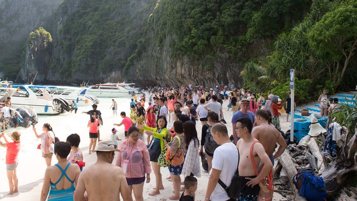 Eine große Anzahl von Touristen an einem weißen Sandstrand.