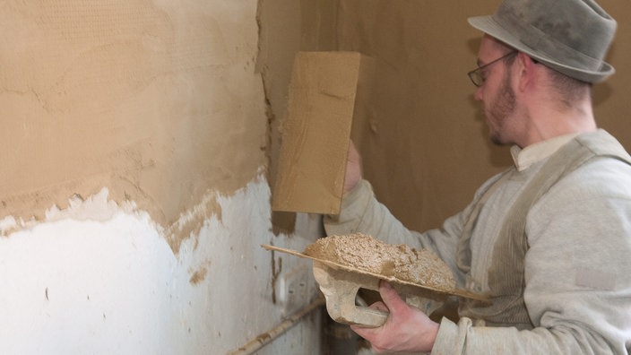 Mann verstreicht Lehmputz auf Hauswand