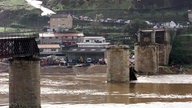 Die Brückenpfeiler ragen aus dem Fluss. Im Hintergrund stehen Massen an Schaulustigen. 