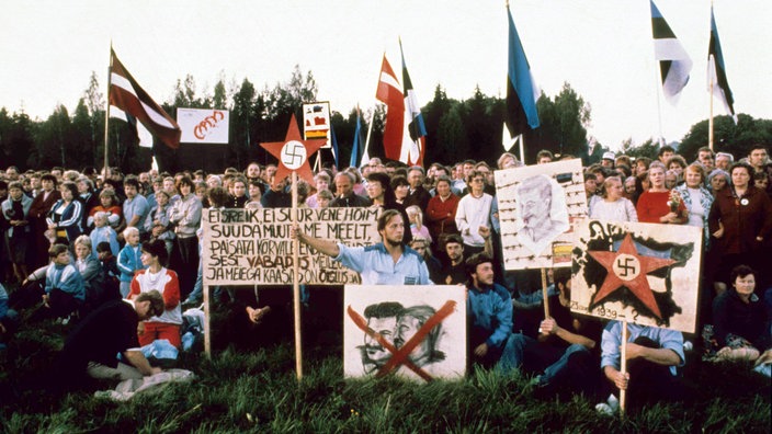 Menschen halten bei einer Demonstration Plakate mit den Köpfen von Hitler und Stalin, die durchgestrichen sind.