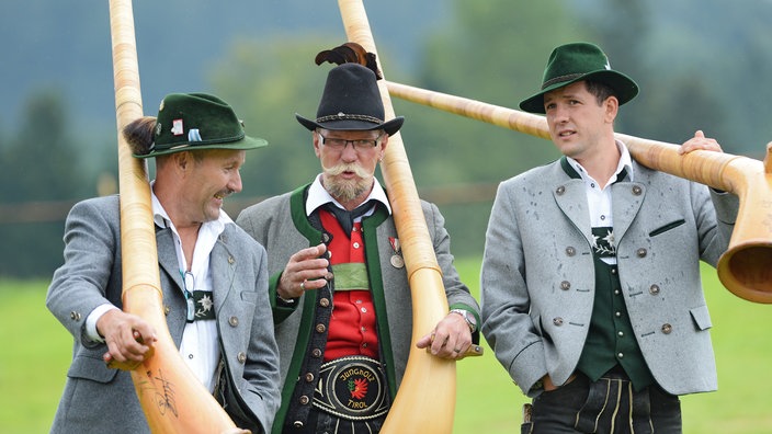 Drei Alphornbläser laufen im Allgäu eine Wiese hinunter