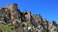 Eine Burgruine steht inmitten von Felsen, die mit Pflanzen bewachsen sind