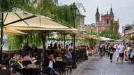 Restaurants am Flussufer, flanierende Menschen, Blick auf eine Kirche im Hintergrund