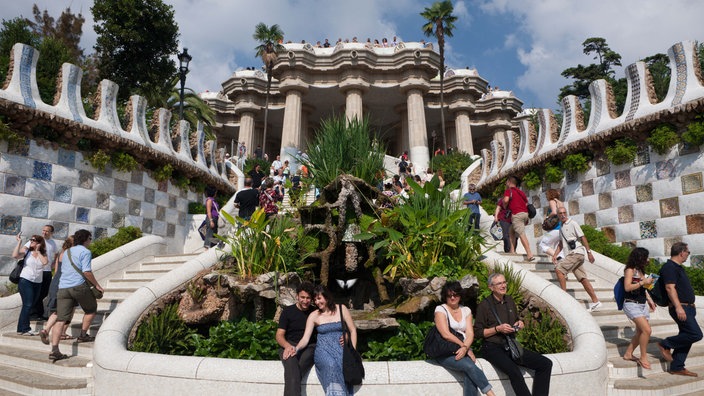 Detailansicht des Parc Güell in Barcelona mit einem geschwungenen Treppenaufgang und Gebäuden mit fließenden Forme