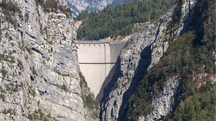 Blick in ein enges Tal, oben eine Staumauer zwischen den Bergen