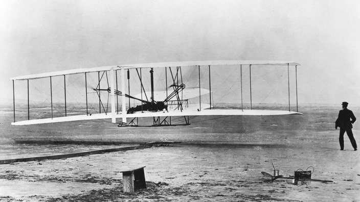 Ein Doppeldecker fliegt knapp über einen Sandboden