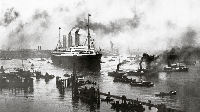 Schwarzweiß-Bild: Ein riesiges Dampfschiff bei der Ausfahrt aus dem Hamburger Hafen