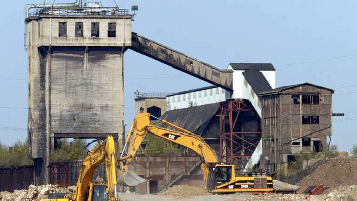 Vor den Überresten des ehemaligen Krupp-Stahlwerks in Duisburg-Rheinhausen tragen Bagger Abbruchmaterial ab.